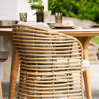 Natural rattan chair with a woven pattern, featuring a soft gray cushion against a bright outdoor setting.