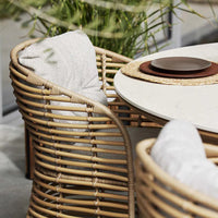 Rattan dining chairs with neutral cushions, circular table with beige tones, and natural textures for a cozy, modern look.