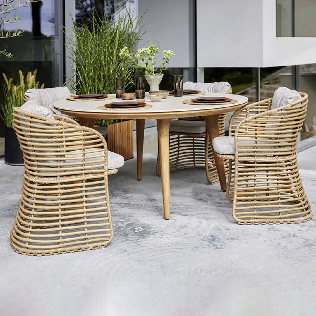 Natural rattan dining set with beige cushions, round table, and unique woven chair patterns. Modern outdoor style.