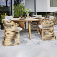 Natural rattan dining set with beige cushions, round table, and unique woven chair patterns. Modern outdoor style.