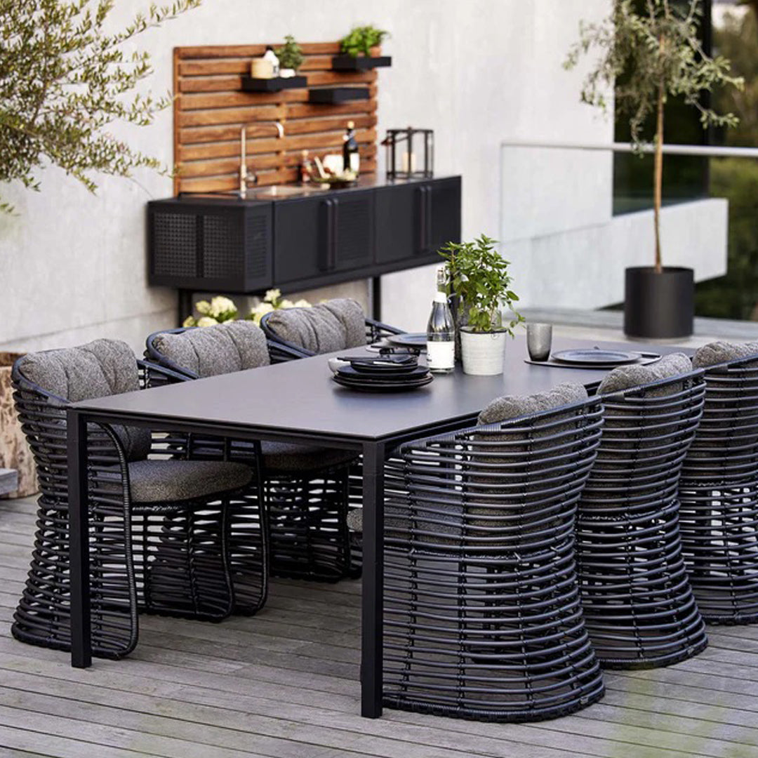 Black woven dining chairs surround a sleek black table, featuring a textured design and natural wood accents in the background.
