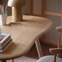 Light oak wood table with smooth curves, featuring earthy tones and a minimalist design in a cozy setting.