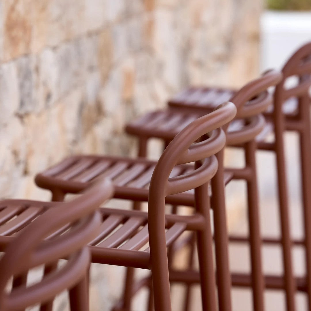 Brown bar stools with a sleek, slatted design against a textured stone wall. Perfect for modern decor.