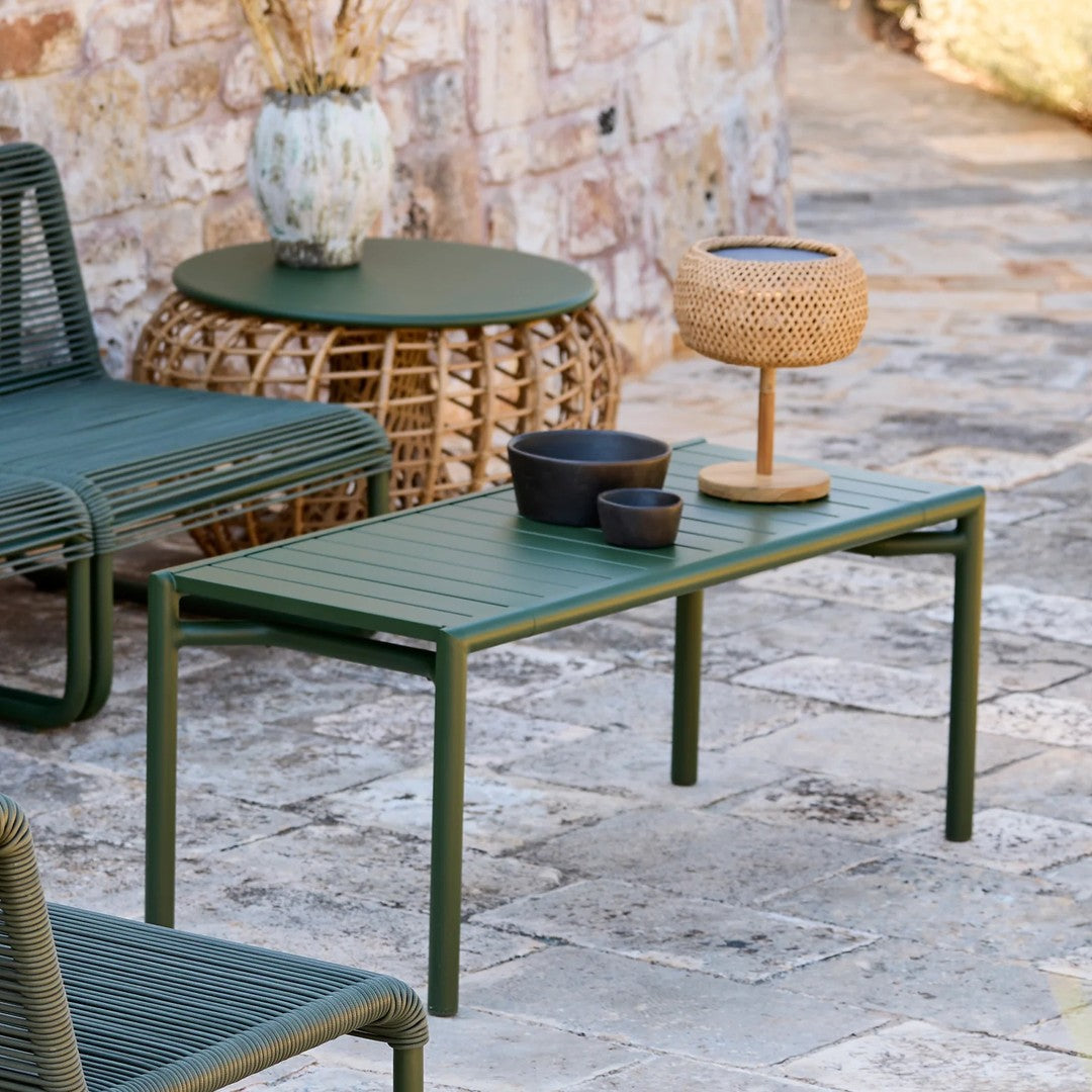 Green slatted outdoor coffee table with minimalistic design, paired with black and natural decor accents.