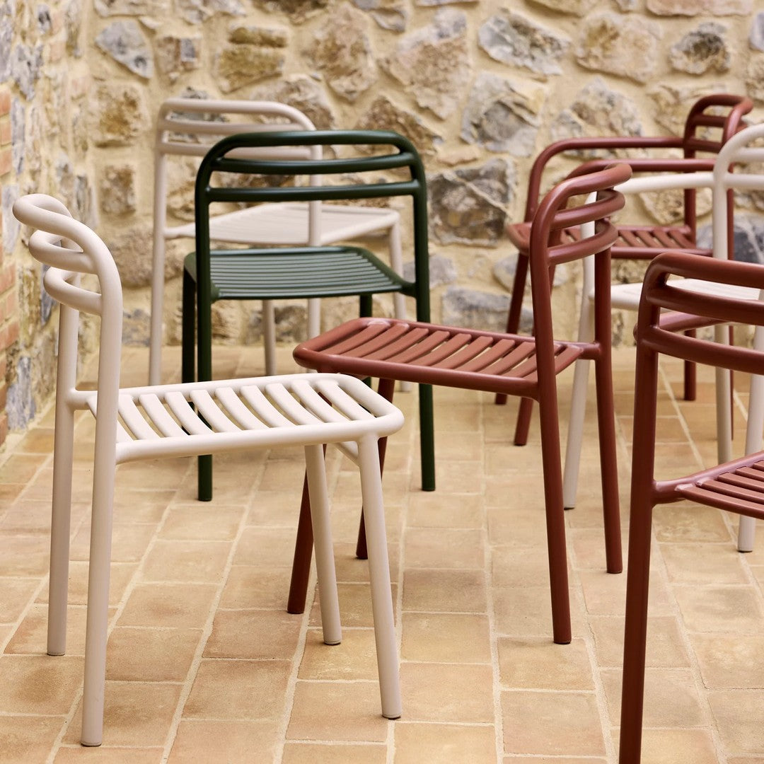 Colorful outdoor chairs in beige, green, and burgundy with sleek slatted designs against a stone wall backdrop.