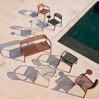 Colorful outdoor chairs in red, green, white, and brown, casting unique shadows on a sunny patio.