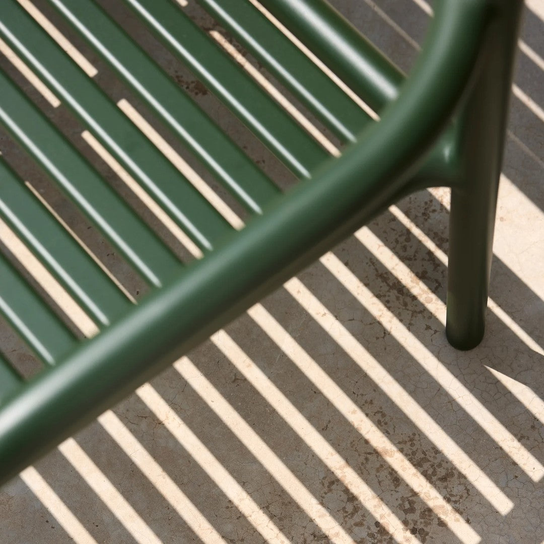 Green metal bench casting striped shadows on a light gray surface. Minimalist design with sleek lines and modern appeal.