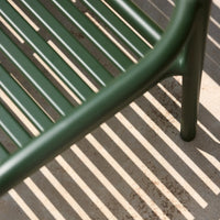Green metal bench casting striped shadows on a light gray surface. Minimalist design with sleek lines and modern appeal.