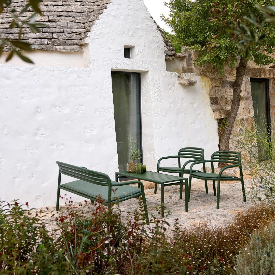Green outdoor seating set with clean lines, complemented by neutral tones of surrounding architecture and lush greenery.