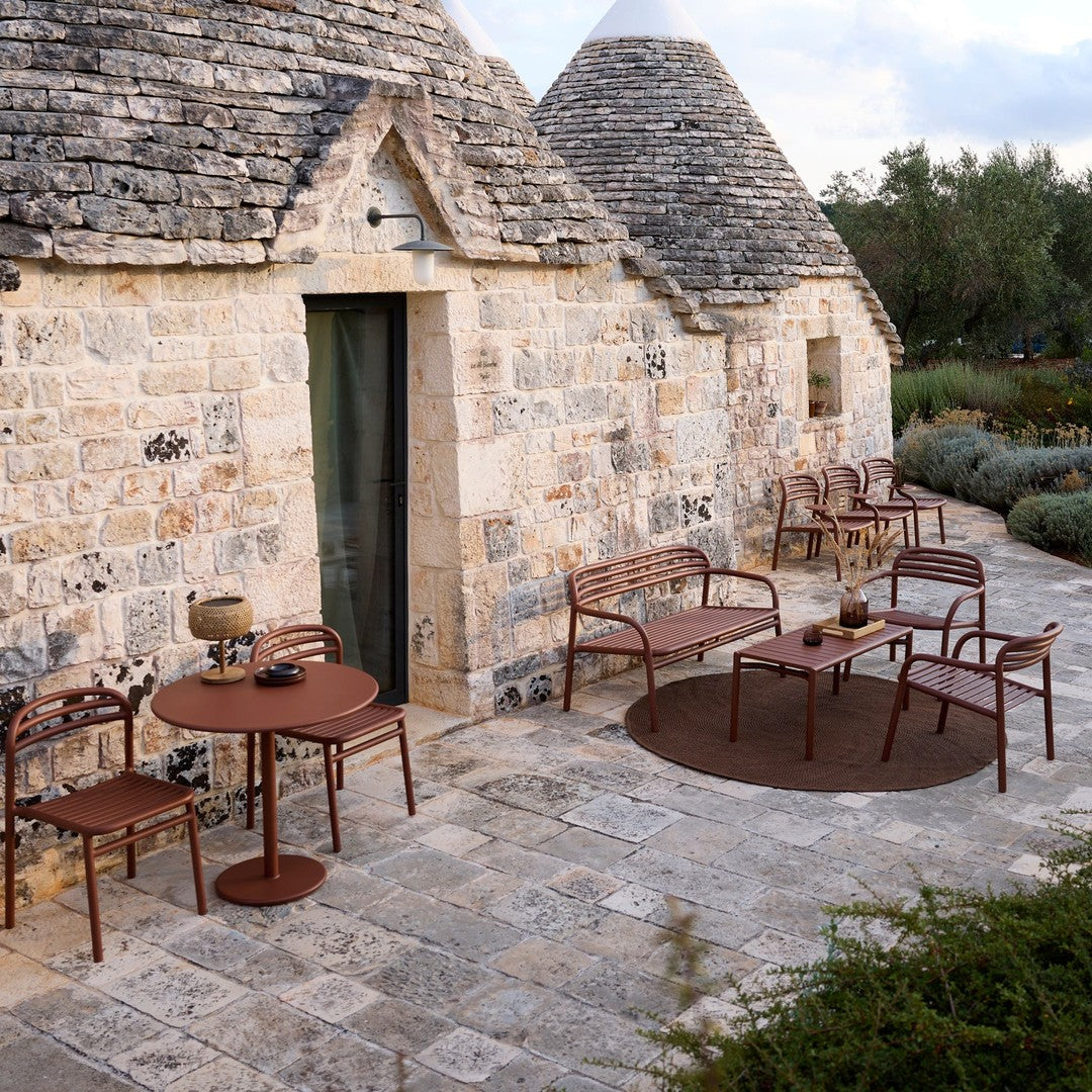 Rust-colored furniture set against rustic stone walls, featuring a round table and chairs with sleek, modern lines.