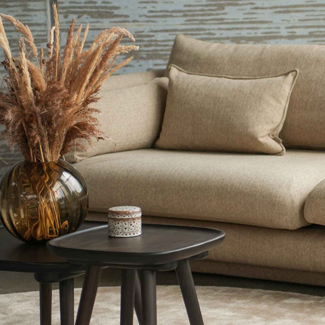 Beige textured sofa with a neutral pillow, dark wood table, and a glass vase filled with dried flowers. Modern cozy decor.
