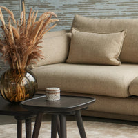 Beige textured sofa with a neutral pillow, dark wood table, and a glass vase filled with dried flowers. Modern cozy decor.
