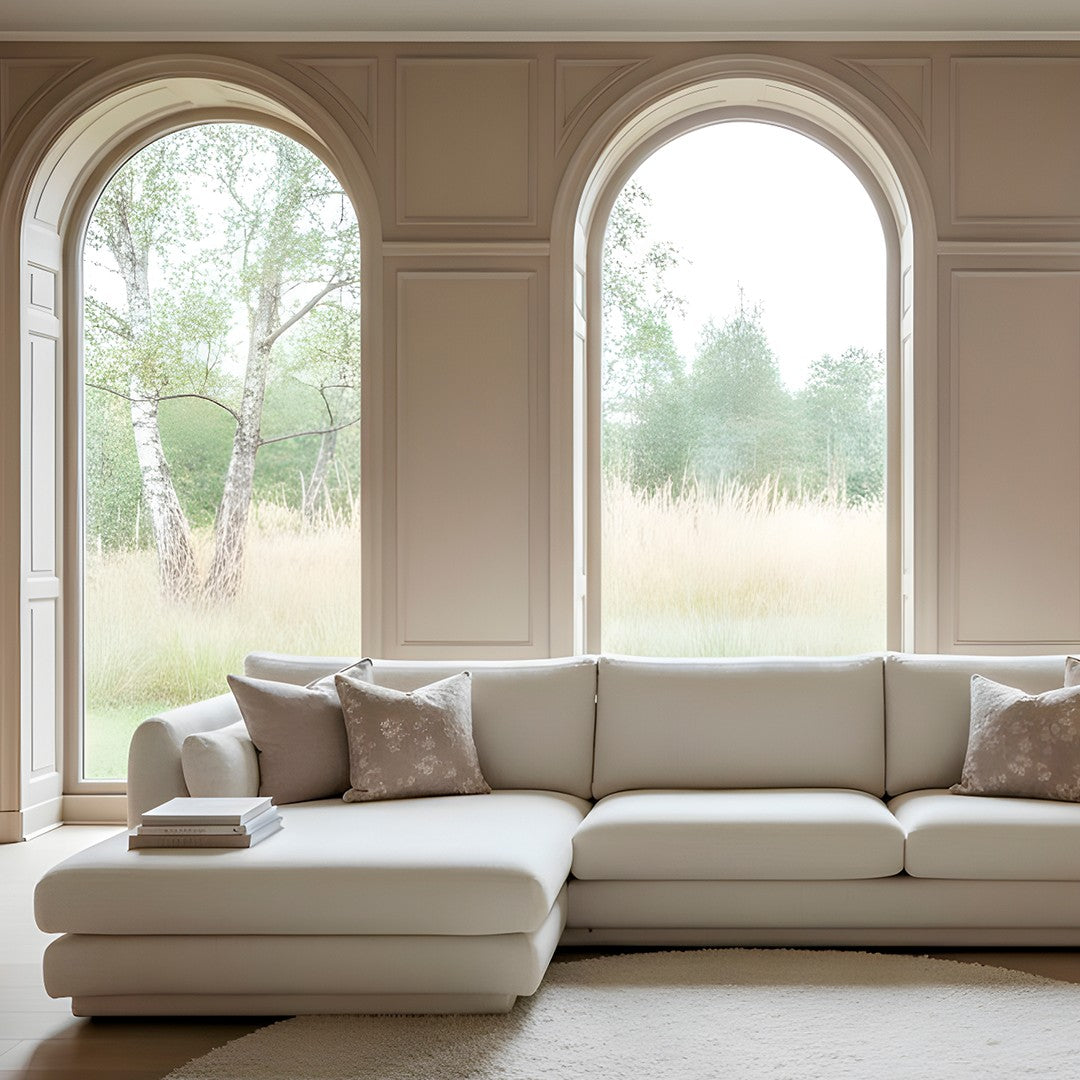 Cream L-shaped sofa with subtle pattern, styled with decorative pillows, set against a minimalistic, natural backdrop.