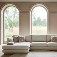 Cream L-shaped sofa with subtle pattern, styled with decorative pillows, set against a minimalistic, natural backdrop.