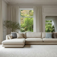 Beige sectional sofa with textured cushions in soft gray and muted earth tones, set against a bright, natural backdrop.