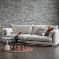 Stylish cream sofa with textured fabric, accented by gray and rust throw pillows, on a round beige rug.