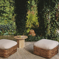 "Natural woven rattan ottomans with light cream cushions, surrounded by lush greenery in a serene outdoor setting."