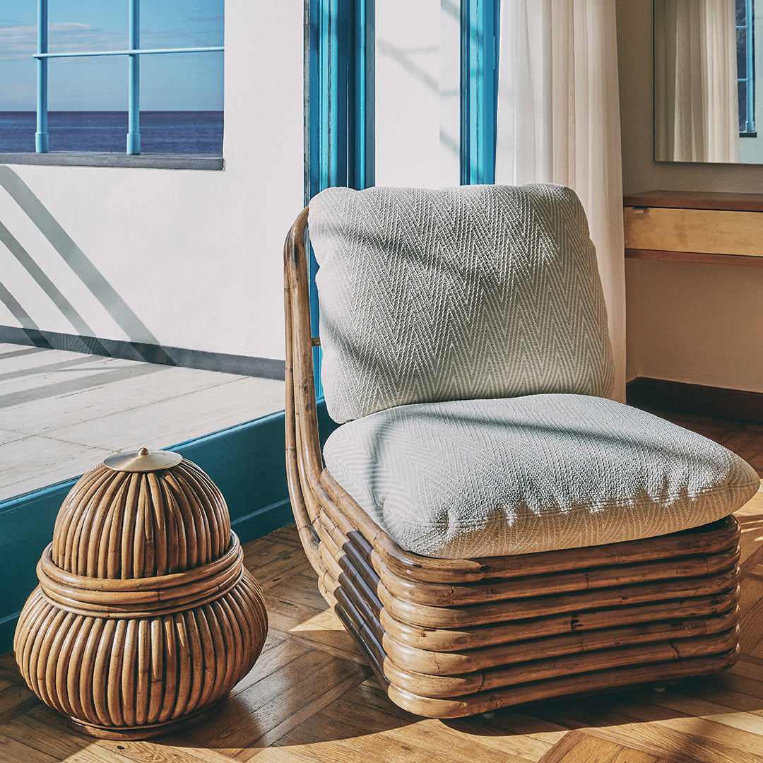 Light gray cushioned chair with woven rattan base, paired with a round bamboo accent table.