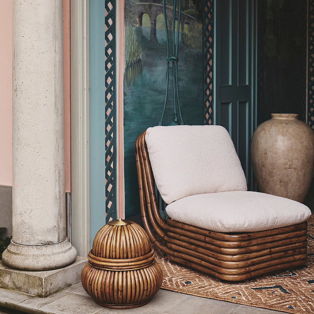 Light beige cushion on a woven rattan chair, paired with a round decorative basket in warm wood tones.