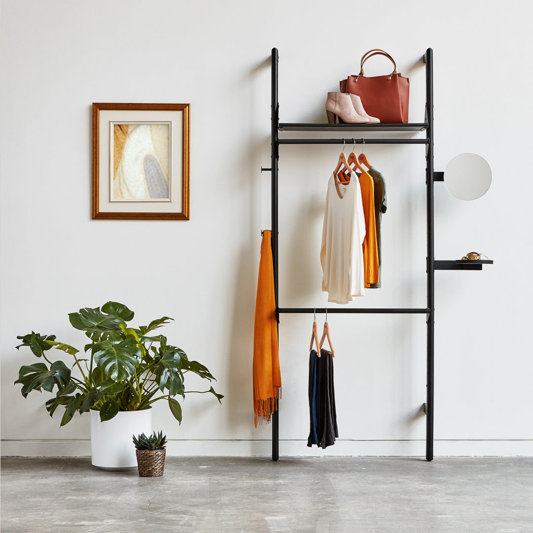 Modern black clothing rack with vibrant orange and yellow garments, accented by a lush green plant and minimalist decor.