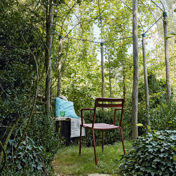 "Red chair with a sleek design against lush green foliage and a soft blue cushion for a vibrant outdoor setting."