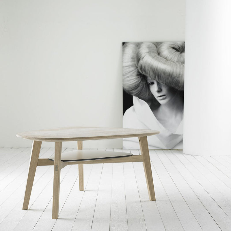 Light wood coffee table with smooth, minimalist design; complemented by a monochrome art piece in the background.