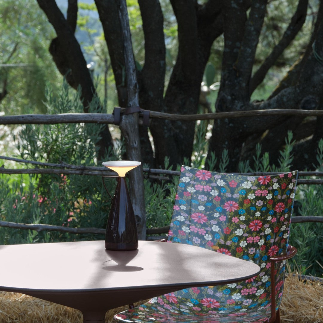 Colorful floral pattern on a chair with pink, blue, and green hues, set against greenery and rustic wood backdrop.