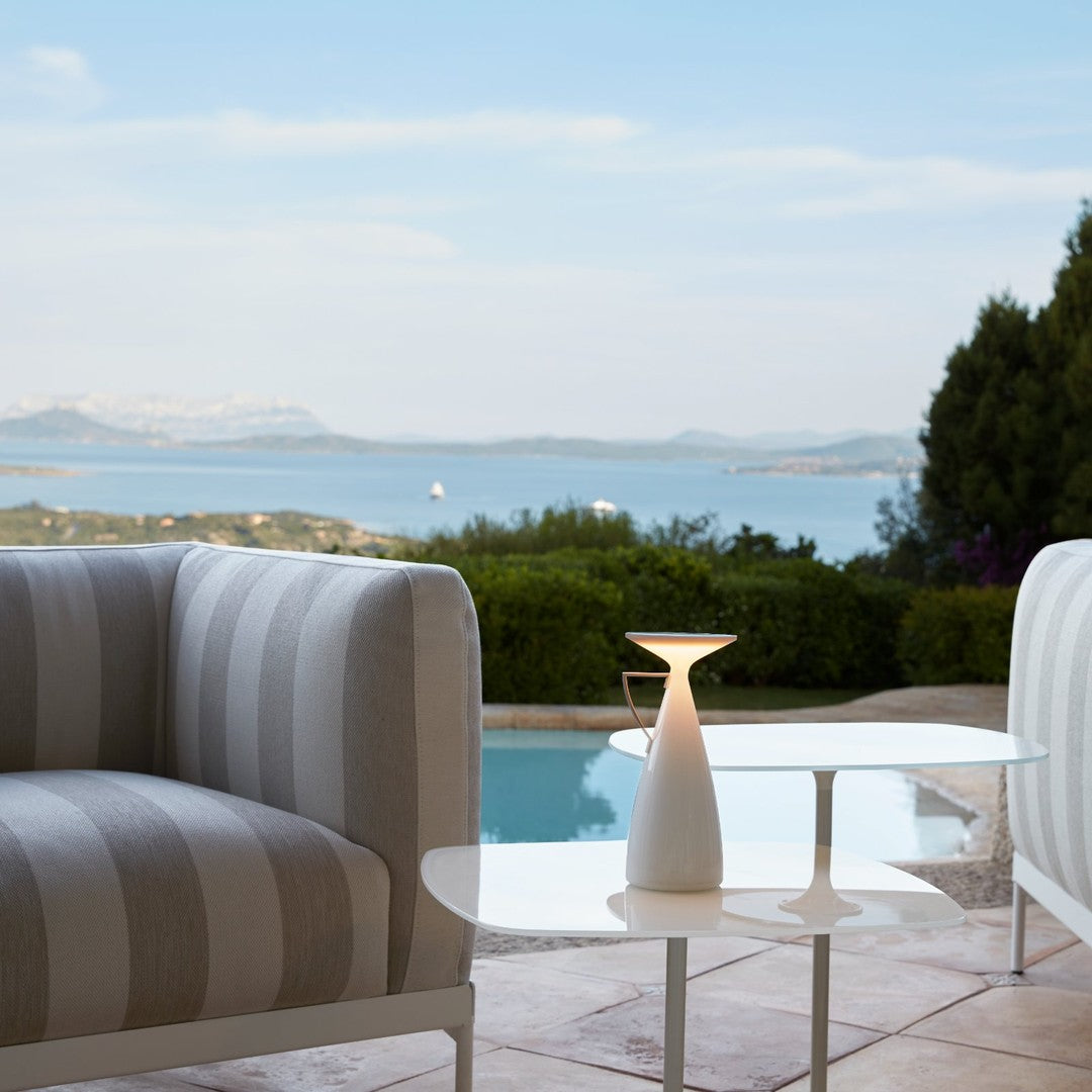 Gray and white striped sofa with a sleek white table, set against a serene outdoor landscape.