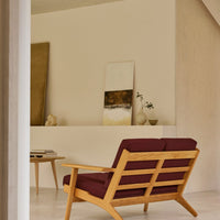 Mid-century modern sofa with deep burgundy cushions and light hardwood frame, set against a neutral background.