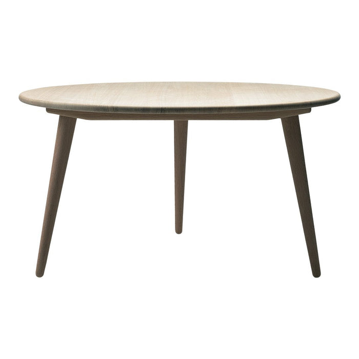 Round wooden table with a light beige surface and contrasting dark brown legs, featuring a sleek, minimalist design.