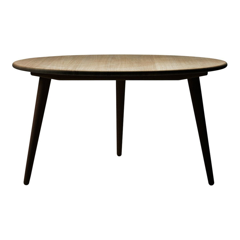Round wooden dining table with a light oak finish and dark tapered legs, showcasing a modern minimalist design.