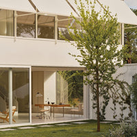 Modern white exterior with large glass windows; lush green grass and vibrant tree add natural elements.
