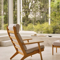 "Light beige cushion on a wooden lounge chair, showcasing a minimalist design against a serene green backdrop."