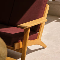"Maroon upholstered sofa with natural wood armrests and a light beige floor background, featuring clean lines."