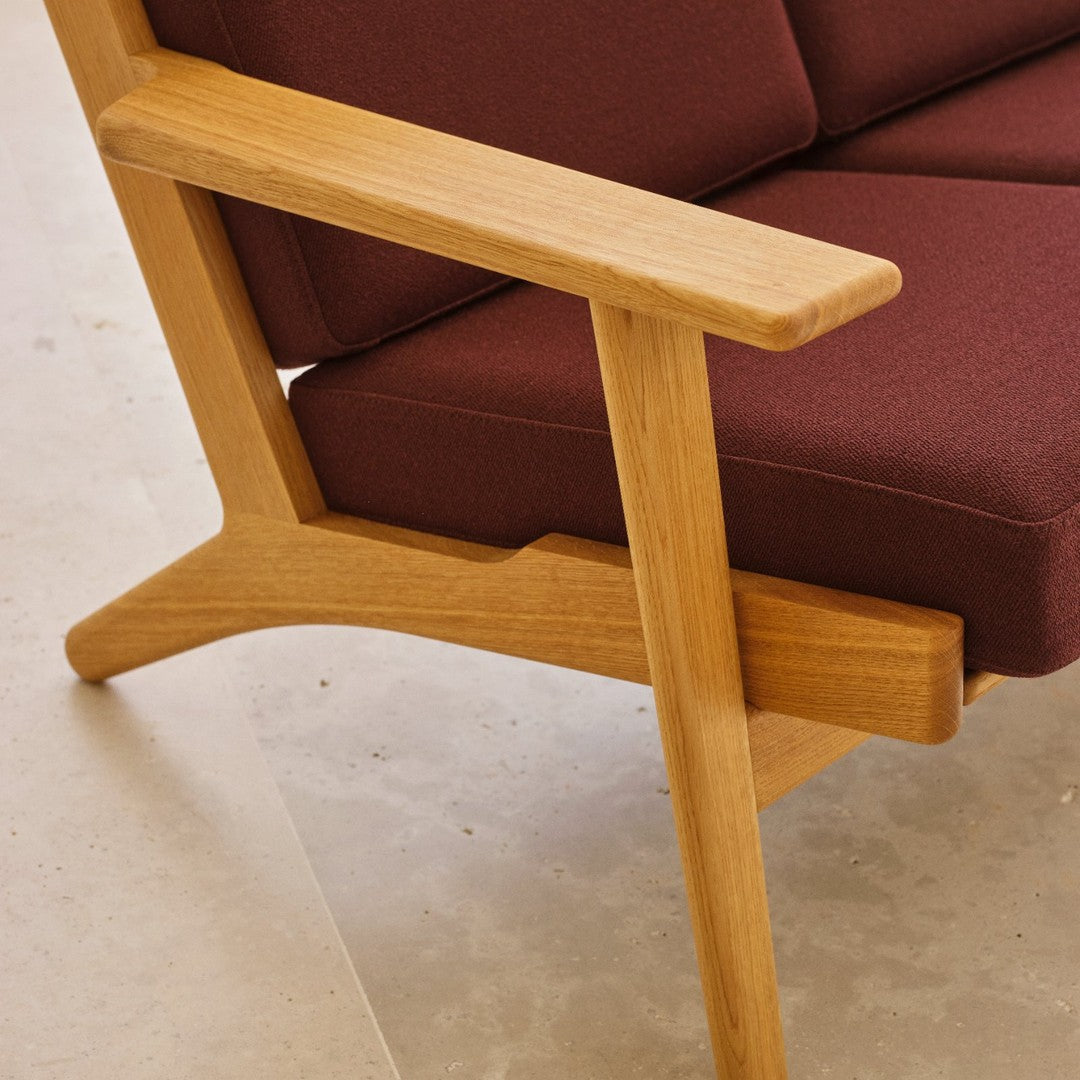 Mid-century modern sofa with rich burgundy upholstery and a natural oak frame, showcasing a sleek, minimalist design.