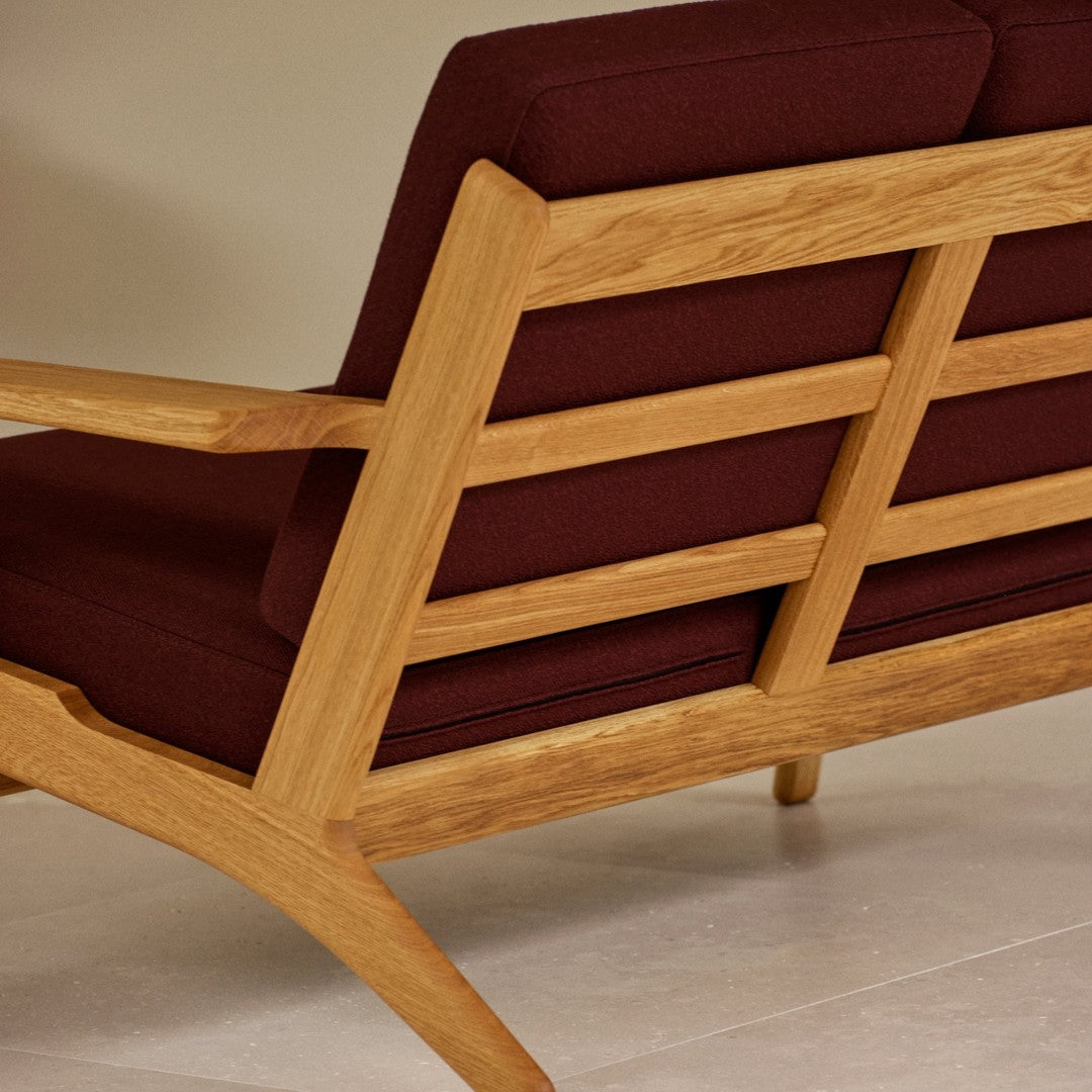Sleek oak frame sofa with rich burgundy cushions, showcasing a modern design with elegant lines and warm tones.