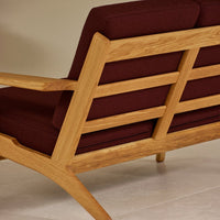 Sleek oak frame sofa with rich burgundy cushions, showcasing a modern design with elegant lines and warm tones.