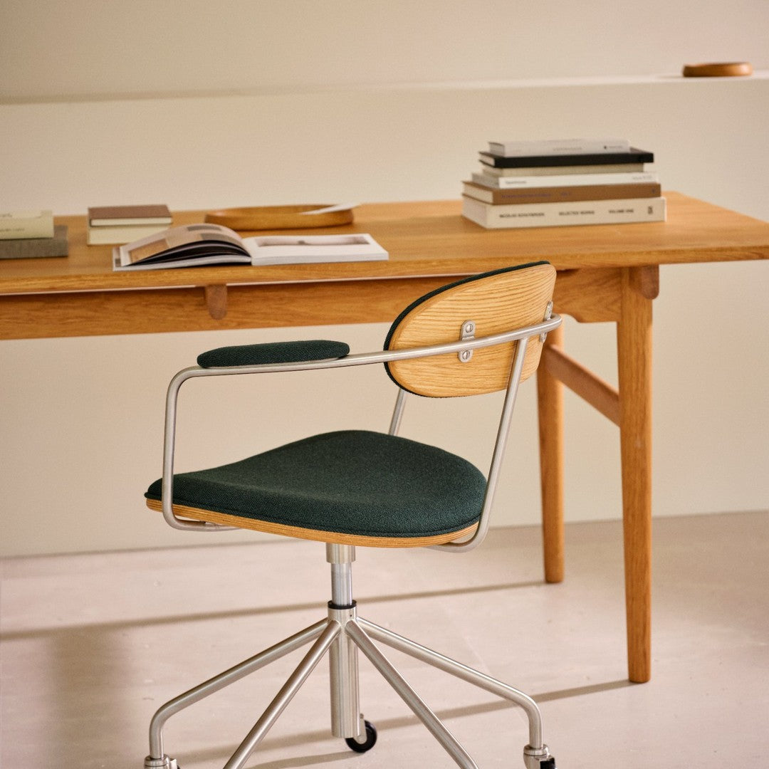 Green upholstered chair with wood accents, placed beside a minimalist wooden desk in a neutral-toned setting.