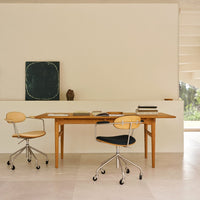 Light wood table with cream and black ergonomic chairs against a neutral wall, featuring subtle textures and muted colors.