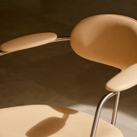 Minimalist beige chair with smooth, rounded seat and armrest, featuring a sleek metal frame. Soft neutral tones and modern design.