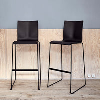 Black modern barstools with sleek lines and minimalist design against a light wood and gray backdrop.