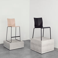 "Minimalist bar stools in blush pink and matte black, displayed on concrete bases against a sleek wall."