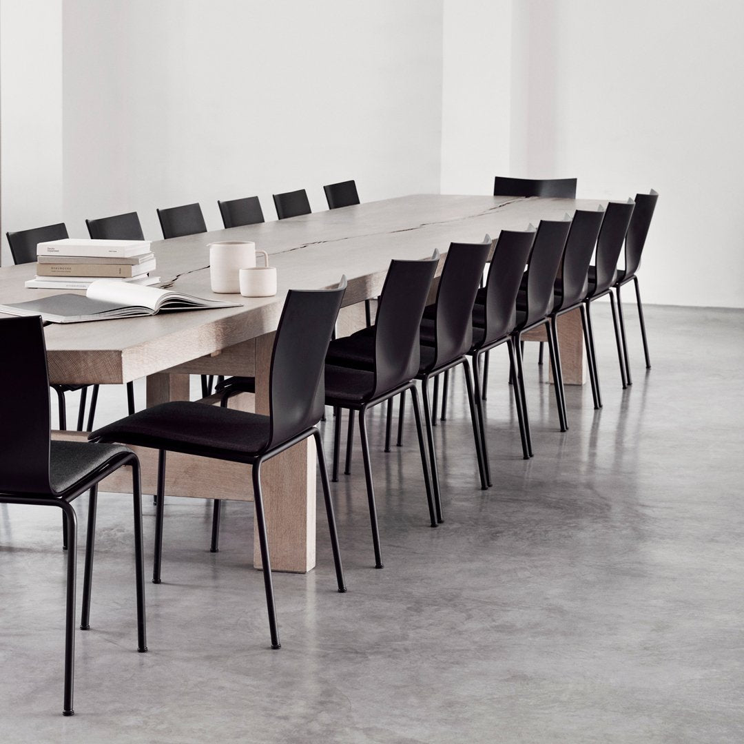 "Modern black chairs around a long light wood table in a minimalist, neutral-toned setting."