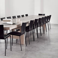 "Modern black chairs around a long light wood table in a minimalist, neutral-toned setting."