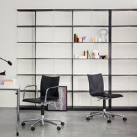 Black ergonomic office chairs on a sleek gray floor, set against a minimalist white wall and geometric black shelving.