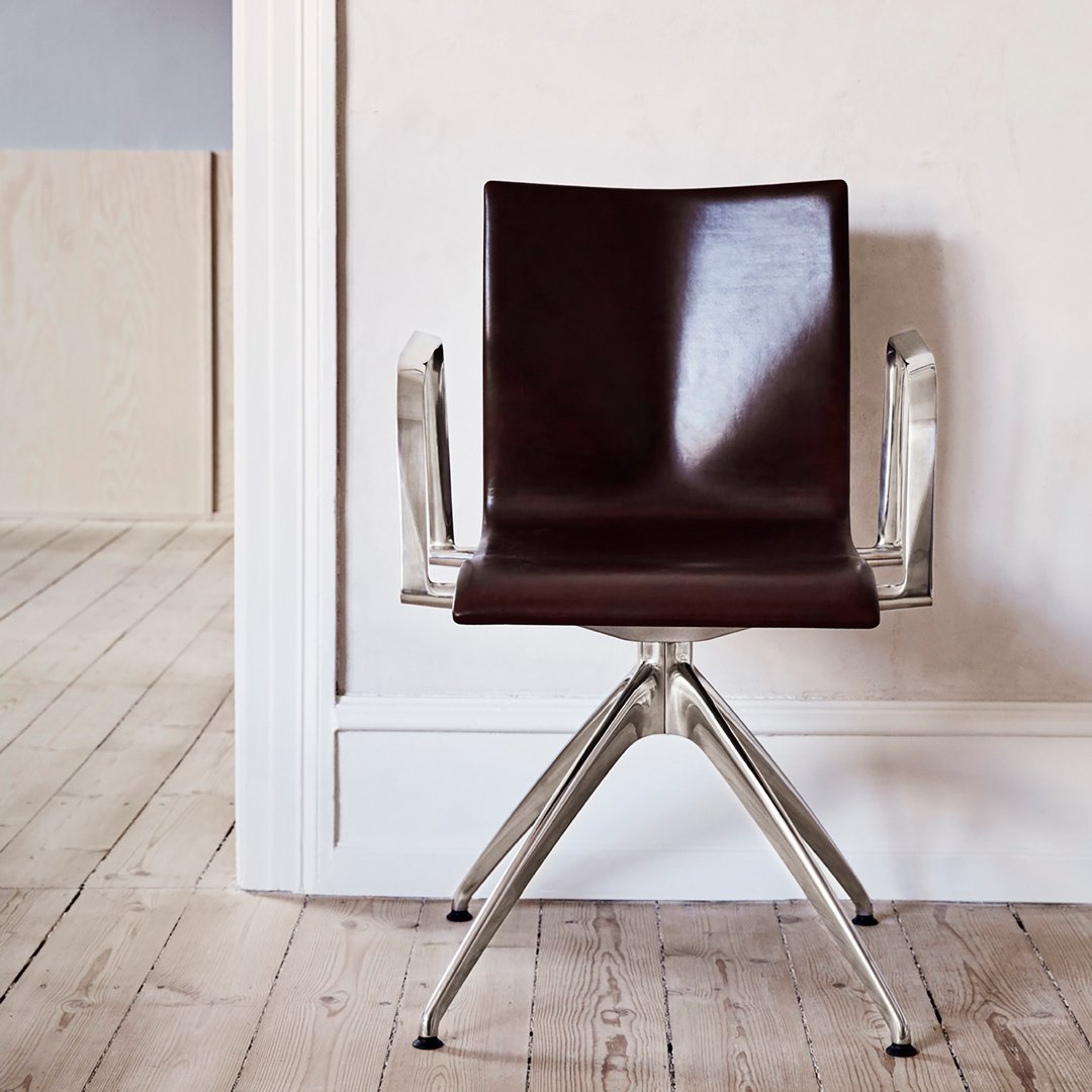 Brown leather chair with sleek chrome arms and a modern, minimalist design on a light wooden floor.