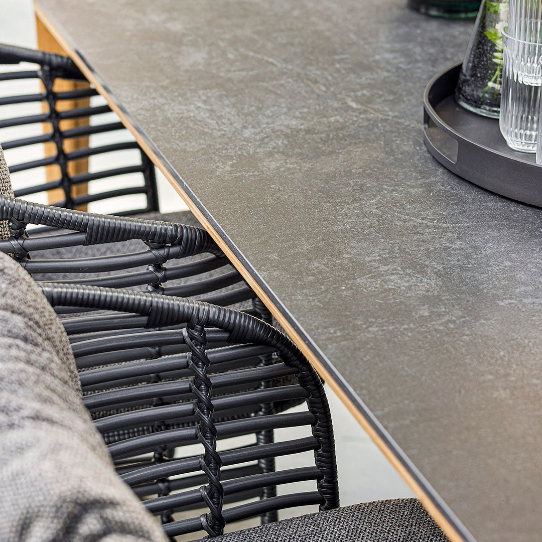Close-up of a textured black tabletop and woven black chair, featuring a soft gray cushion. Elegant and modern design.