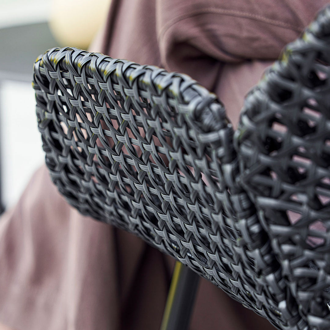 Black woven chair back design featuring intricate patterns against a soft brown backdrop.