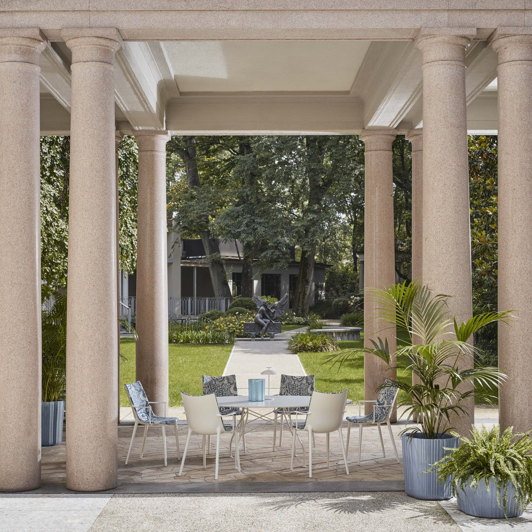 Stylish outdoor dining set featuring gray cushions, white chairs, and a light blue table centerpiece in a serene garden setting.