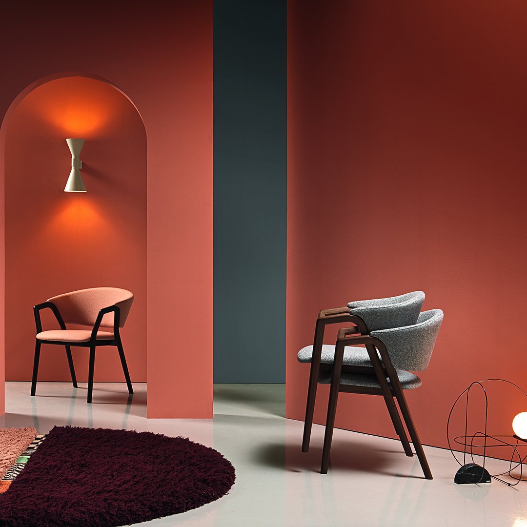 Gray and blush chairs against rich coral and deep blue walls, complemented by a plush burgundy rug. Modern pattern mix.
